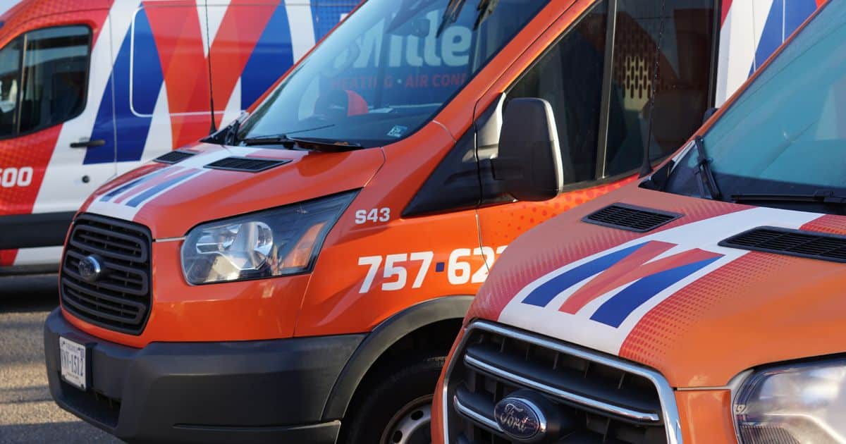 Three vans parked side by side, each painted in vibrant colors of orange, blue, and white. The vans are branded with the logo of Millers Heating & Air Conditioning, with the company name prominently displayed on the sides. The colors of the vans reflect the brand's distinctive color scheme, creating a cohesive and recognizable look.